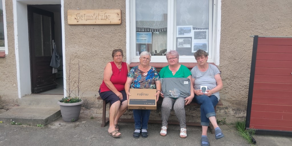 Vier Frauen auf der Bank vor der Heimatstube Sophienhof mit einem Laptop in der Hand