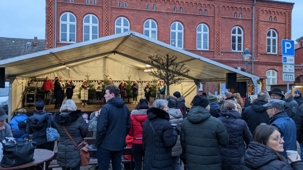Offenes erleuchtetes Festzelt mit Publikum davor, im Hintergrund das Amtsgebäude von Loitz beim Adventsmarkt